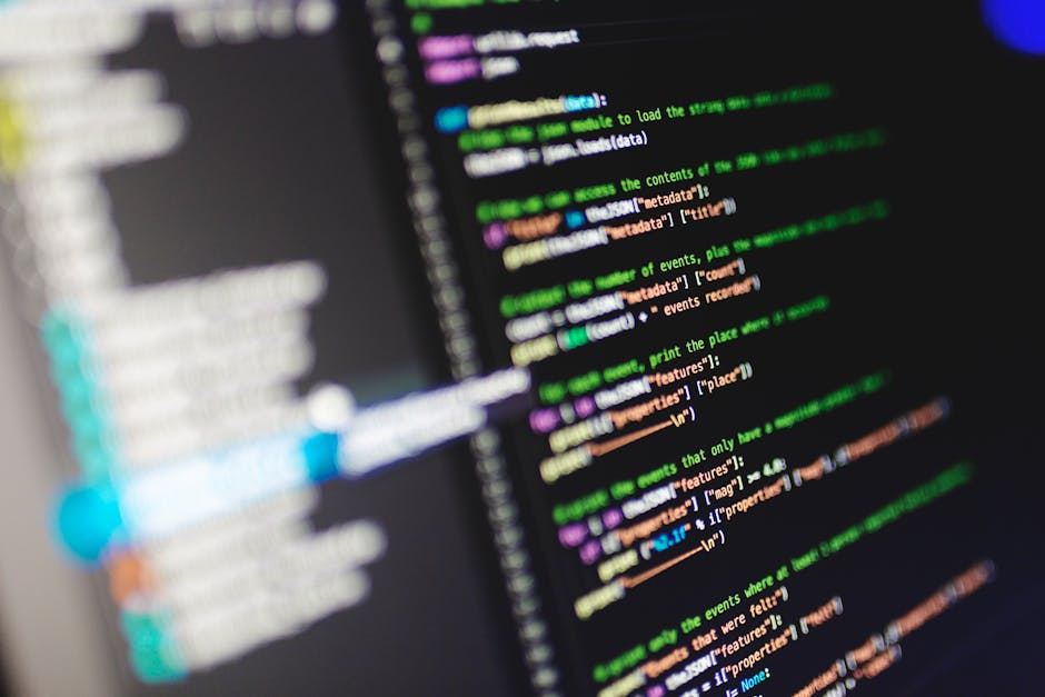 Close-up photograph of a computer screen displaying lines of code with syntax highlighting in various colors such as green, purple, orange, and blue on a dark background. The text appears slightly blu